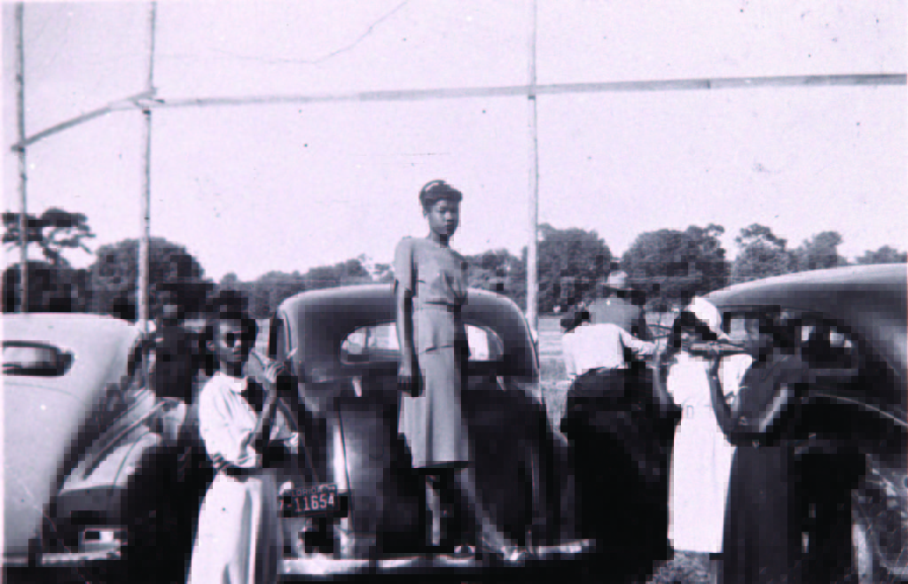[Baseball fans on cars image] Baseball was a favorite Sunday afternoon pastime – after church, fans headed to the games. In this 1940s photograph, four stylishly dressed women are socializing and enjoying soft drinks in the backfield. The young woman standing at left is our cousin Shirley Mitchell Jackson. The baseball team sold soft drinks, peanuts and other snacks during the games to raise money for equipment and uniforms. The playing field was in a swampy area on the current site of Winter Park Village, along Webster and Denning avenues. Peggy Collins Hall Native of Winter Park March 5, 2016